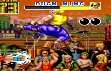 Shows muscle man wearing yellow top and blue trousers and brown boots on doing jumping kick left here and shows on the right hand screen showing arm punching with red t-shirt on it and arange of people showing here and man name doing the kick is called Duck King