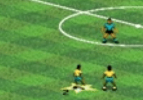 Football match showing two players on the bottom wearing yellow and light blue coloured strip I think meant to look bit like brazil but the 16 bit could not do the country colour right here. The other team top is light blue with black shorts on you see half of the centre of the pitch here showing  darker and light green squares to represent the match playing area and one of the players has n...